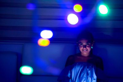 Portrait of smiling young woman against wall with illuminated lighting equipment