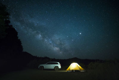 Car parked by illuminated tent against starry sky at night