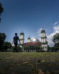 Man standing by building against blue sky