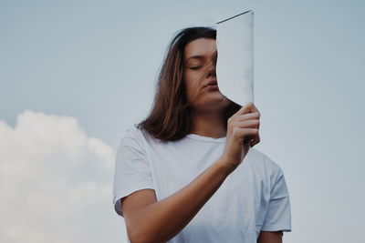 Low angle view of young woman holding mirror against sky