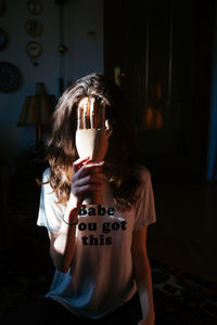 Young woman hiding face with wooden hand at home