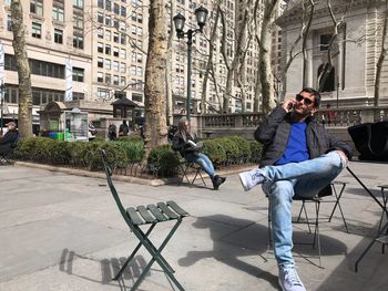 Man talking on phone while sitting on chair in city