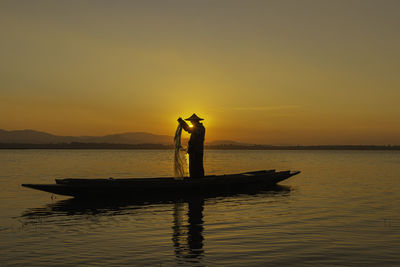 Silhouette man standing on boat in sea against sky during sunset