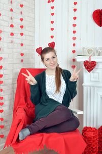Portrait of smiling woman gesturing peace sign while sitting in decorated home