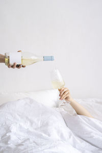 Hand pouring wine in wineglass held on bed at home