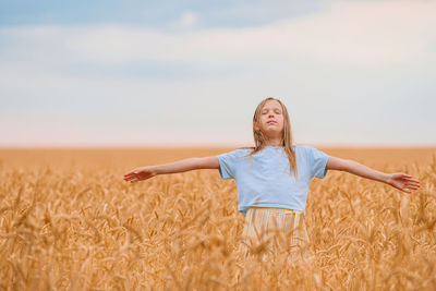 Girl with arms outstretched standing on wheat field