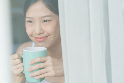 Smiling woman holding coffee cup seen through glass window