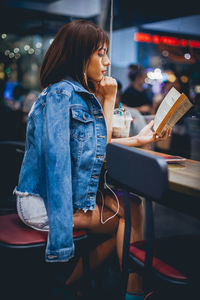 Side view of young woman reading book on restaurant table