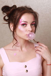 Close-up of beautiful woman with make-up blowing bubble gum against wall