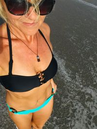 Midsection of woman in bikini standing at beach