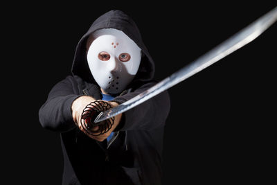 Portrait of man holding mask against black background