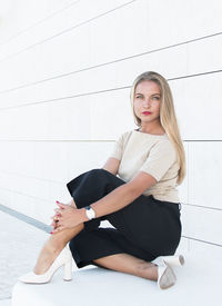 Portrait of beautiful woman sitting against white wall