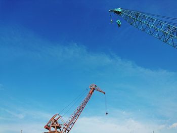 Low angle view of cranes against blue sky