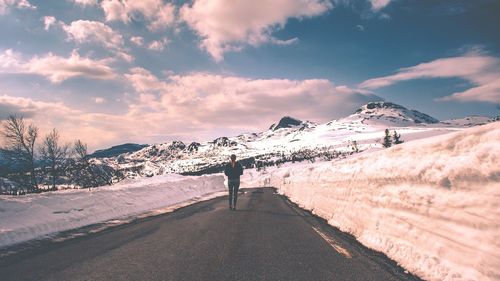 Rear view of man standing on road by snowcapped mountains against sky