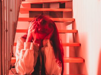 Blurred motion of woman with headache sitting on steps at home