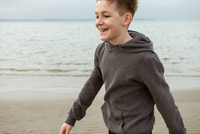 Smiling boy walking on beach against sky