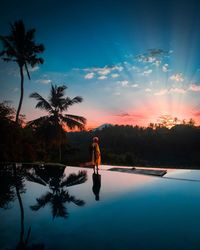 Woman in swimming pool against sky at sunset