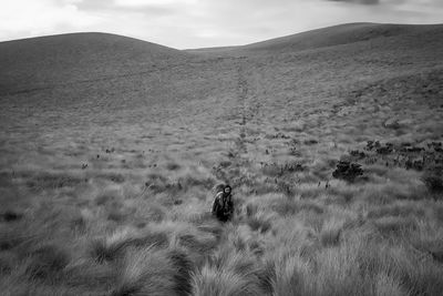 Man walking amidst grassy field against mountains