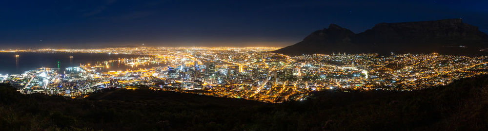 Illuminated cityscape by sea against sky at night