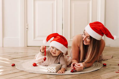 Happy family, cute mom and baby little daughter in santa hats celebrate christmas together at home