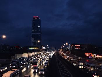 Traffic on road by buildings against sky at night