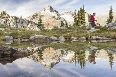 Side view and reflection of backpacker hiking beside alpine lake.