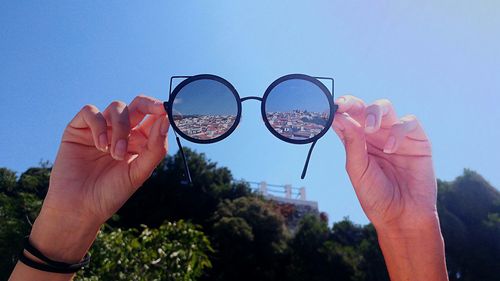 Cropped hands holding sunglasses with houses reflection