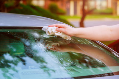 Cropped hand of woman cleaning car windshield