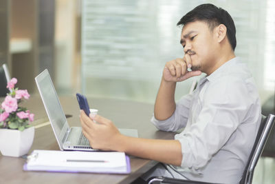 Side view of man using mobile phone at table