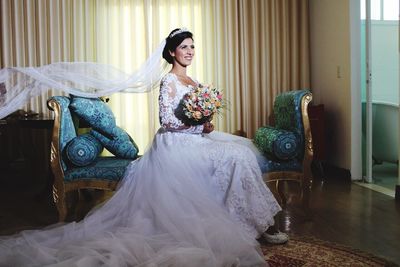 Bride holding bouquet standing on sofa at home