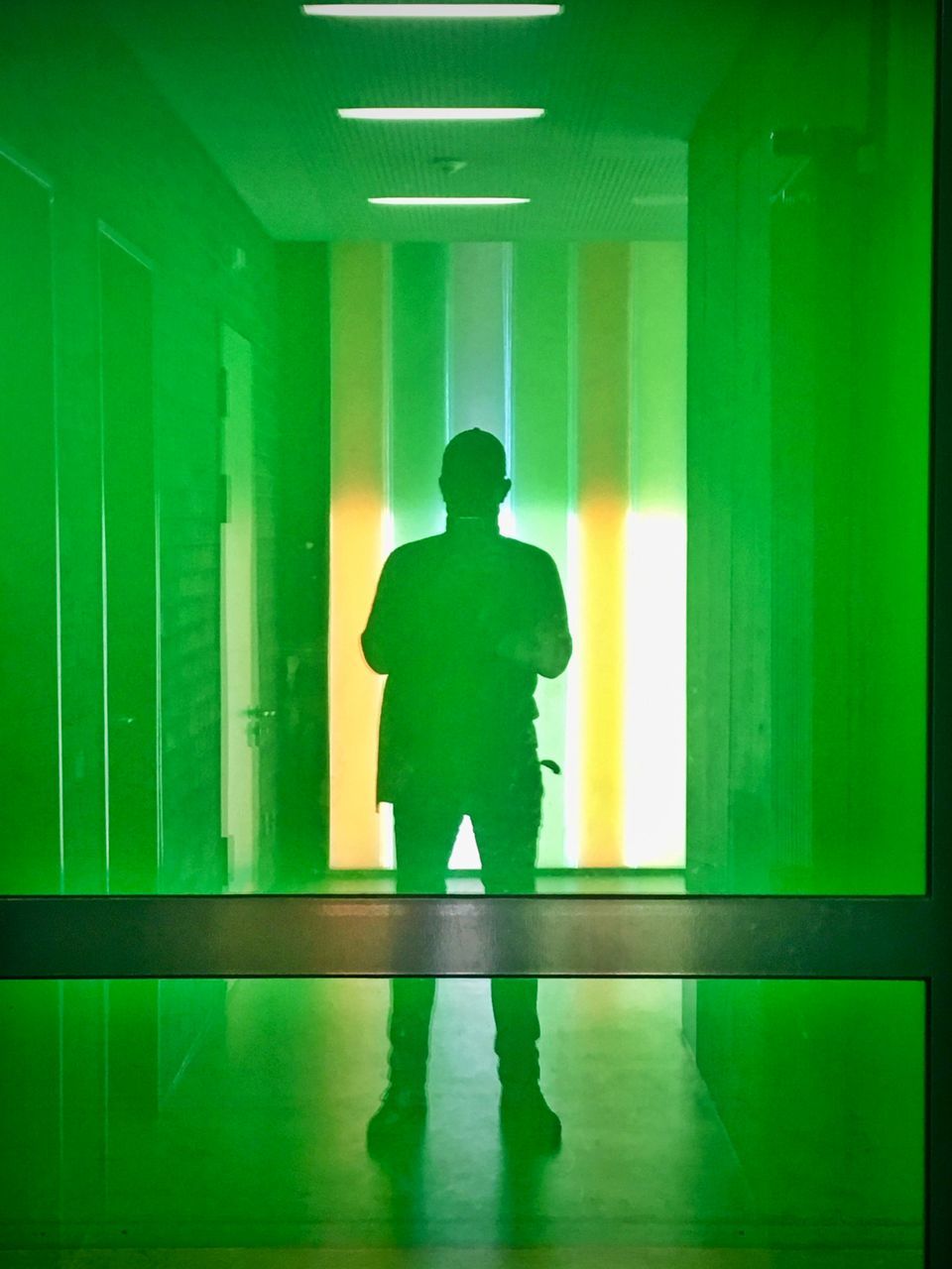 one person, real people, indoors, architecture, green color, standing, men, illuminated, full length, reflection, flooring, rear view, building, built structure, arcade, auto post production filter, corridor, silhouette, lifestyles