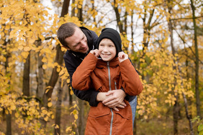 Dad hugs a child who adjusts his hat and laughs