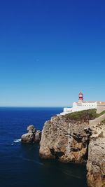 Lighthouse on rocks against clear blue sky