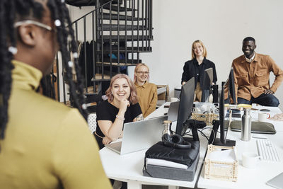 Smiling colleagues looking at businesswoman during meeting in office