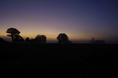 Silhouette trees on field against clear sky at sunset