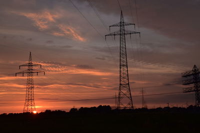 Low angle view of silhouette electricity pylon on field against sky at sunset