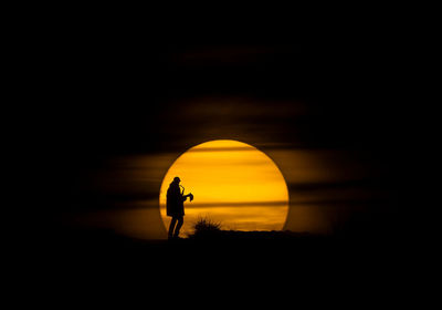 Silhouette person standing against orange sky