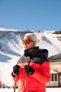 Una mujer afroamericana con bastones de esquí de pie en una montaña nevada durante el invierno