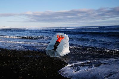 Full length of woman lying on ice by sea at beach against sky during winter