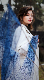 Portrait of beautiful young woman holding scarf standing in forest