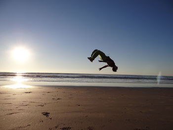 Full length of man backflipping at sandy beach against clear sky