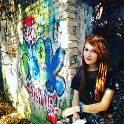 Portrait of smiling young woman standing against graffiti wall