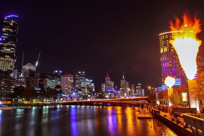 Illuminated buildings by river against sky at night