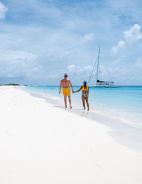 Rear view of woman standing at beach against sky