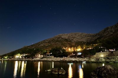 Illuminated buildings by mountains against sky at night