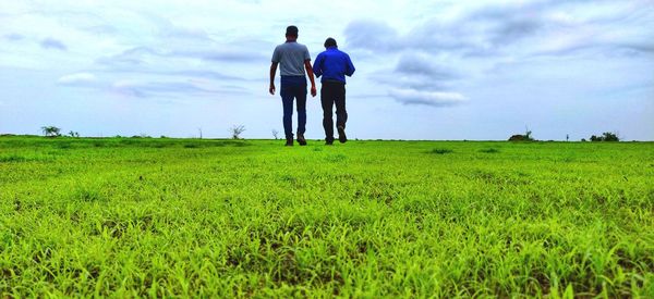 Rear view of men standing on field against sky