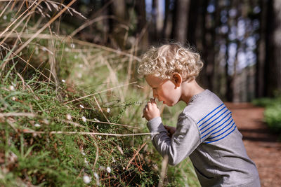 Curly haired boy smelling flowers in forest