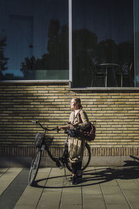 Businesswoman with bicycle standing in front of wall