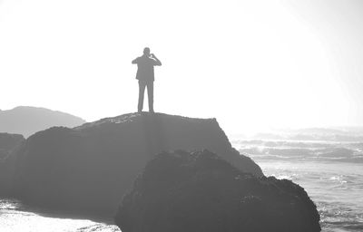 Silhouette man standing on cliff by sea against sky