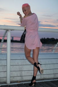 Full length of woman standing by railing against sky during sunset